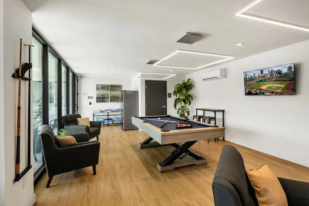 A modern, casual clubhouse interior featuring a pool table, television, cozy seating, and lively indoor plants—ready for groups to gather, unwind, and enjoy game nights together.