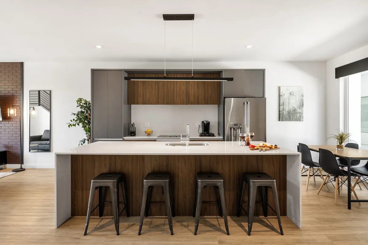 A beautifully lit open kitchen and dining area with a modern island featuring bar stools, premium appliances, and a spacious dining table in view. The arrangement encourages guests to transition seamlessly between cooking, dining, and socializing.