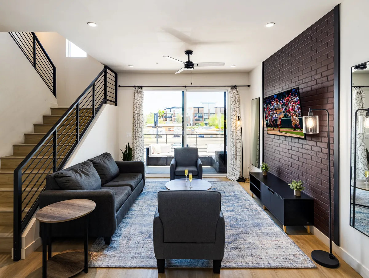 This image features a comfortable, modern living room with a plush sofa, a sleek coffee table, a large flat-screen TV, and expansive windows that fill the space with natural light. The setup encourages relaxation and socializing, with ample room for gatherings and entertainment.