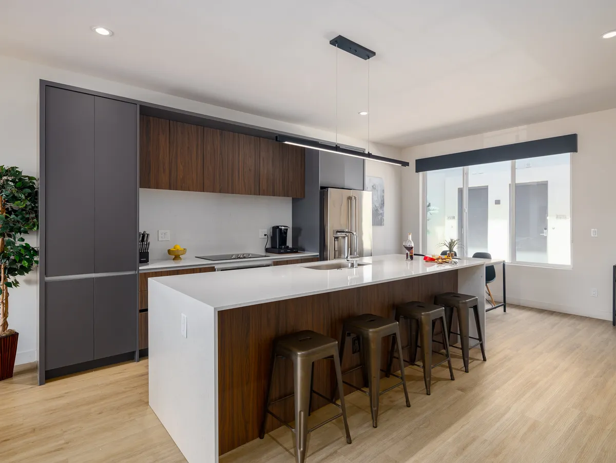 A bright and contemporary kitchen area with an island countertop, stools, window view, and stylish cabinetry. The space is designed for both cooking and casual socializing.